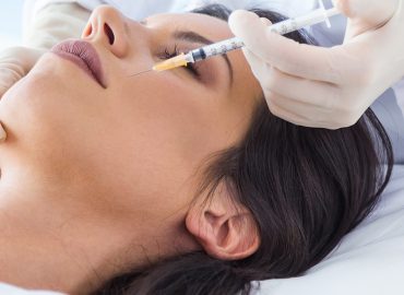 Sanitario con jeringuilla inyectando botox a una mujer jóven en la cara