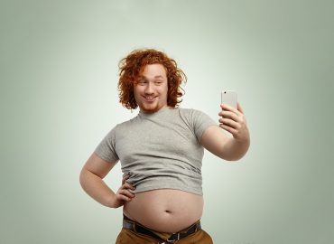 Hombre grueso, caucásico y pelirrojo sacándose un selfie con el móvil