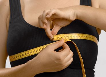 Una mujer joven caucásica se se mide el pecho con un metro de costurera