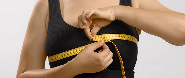 Una mujer joven caucásica se se mide el pecho con un metro de costurera